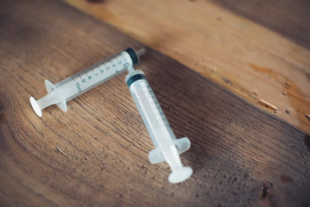 white and black plastic syringe on brown wooden table