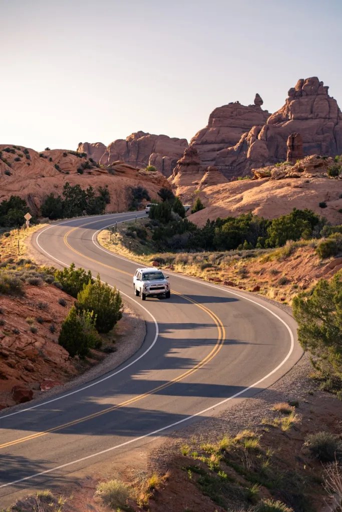 A silver SUV driving on a winding road through a red rock desert landscape